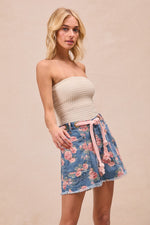 Woman wearing a strapless top and floral skirt on a beige background