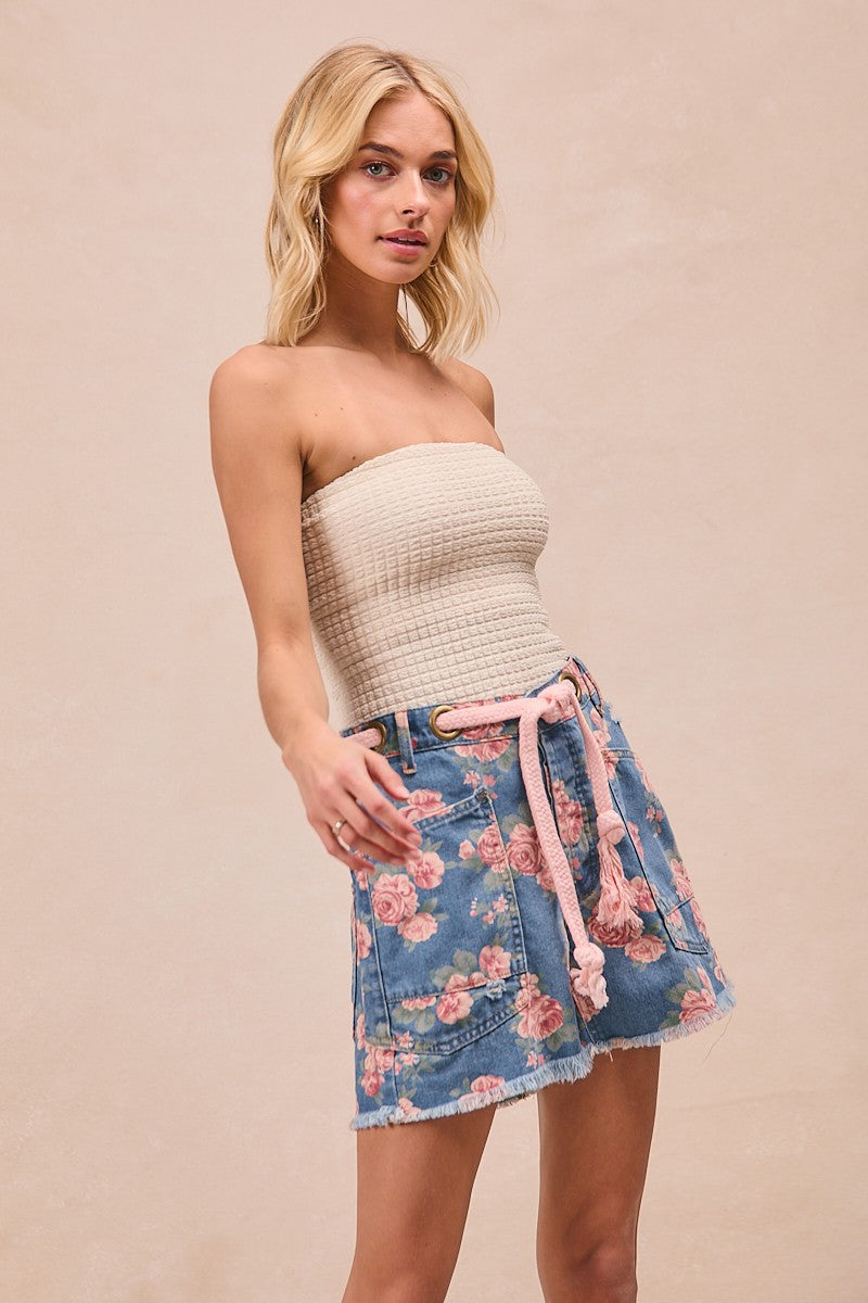 Woman wearing a strapless top and floral skirt on a beige background