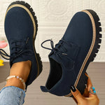 Navy blue shoes with thick soles held by a person against a textured white wall.