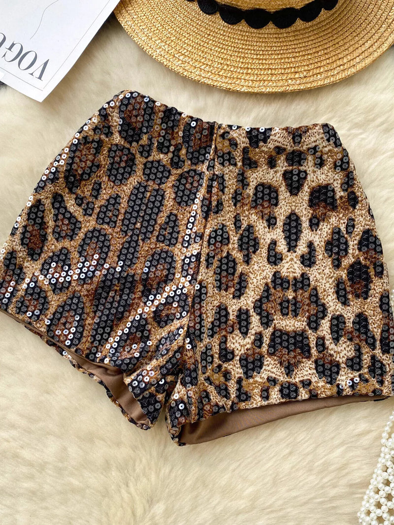 Leopard print sequin fabric on a textured surface with a straw hat in the background.