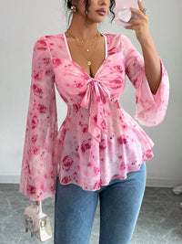 Woman wearing a pink floral blouse and blue jeans, taking a mirror selfie.