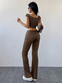 Woman wearing a brown outfit standing against a white wall.