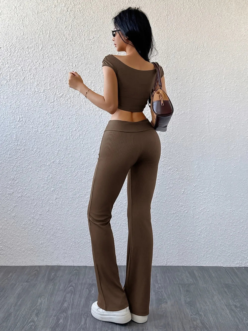 Woman wearing a brown outfit standing against a white wall.