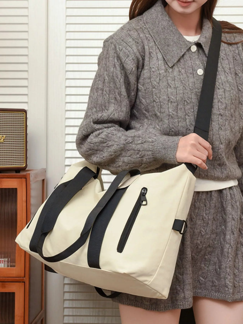 Person wearing a gray cable knit sweater and holding a beige bag with black straps.