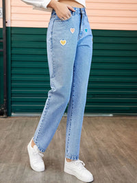 Person wearing light blue jeans with heart patches in front of a green door.