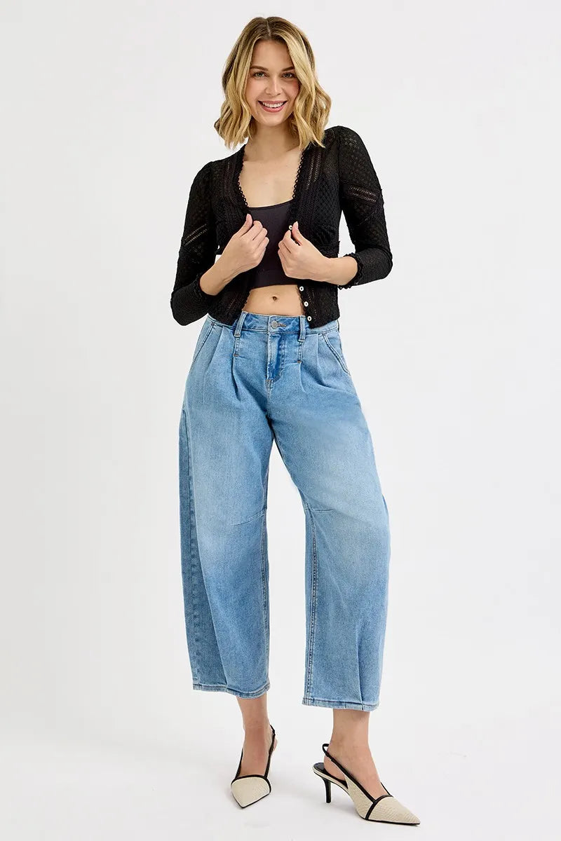 Woman wearing a black cropped jacket, black top, and light blue jeans on a white background