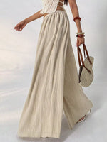 Person wearing a white top and beige wide-leg pants, holding a straw bag on a light background