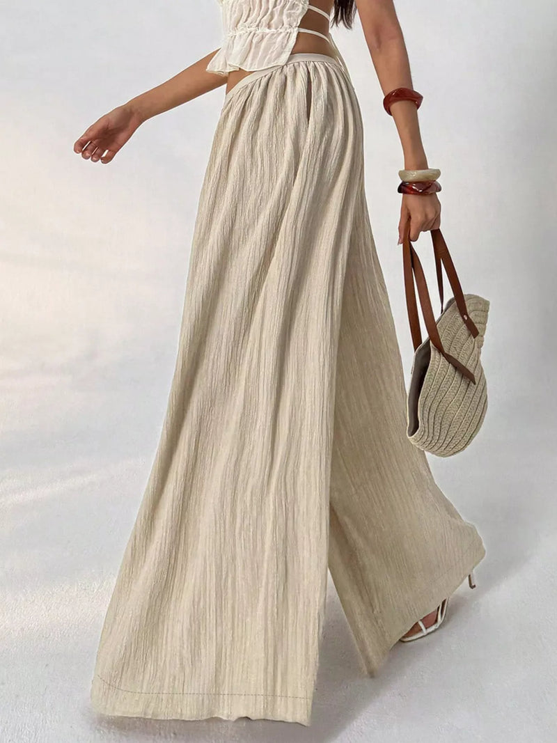 Person wearing a white top and beige wide-leg pants, holding a straw bag on a light background
