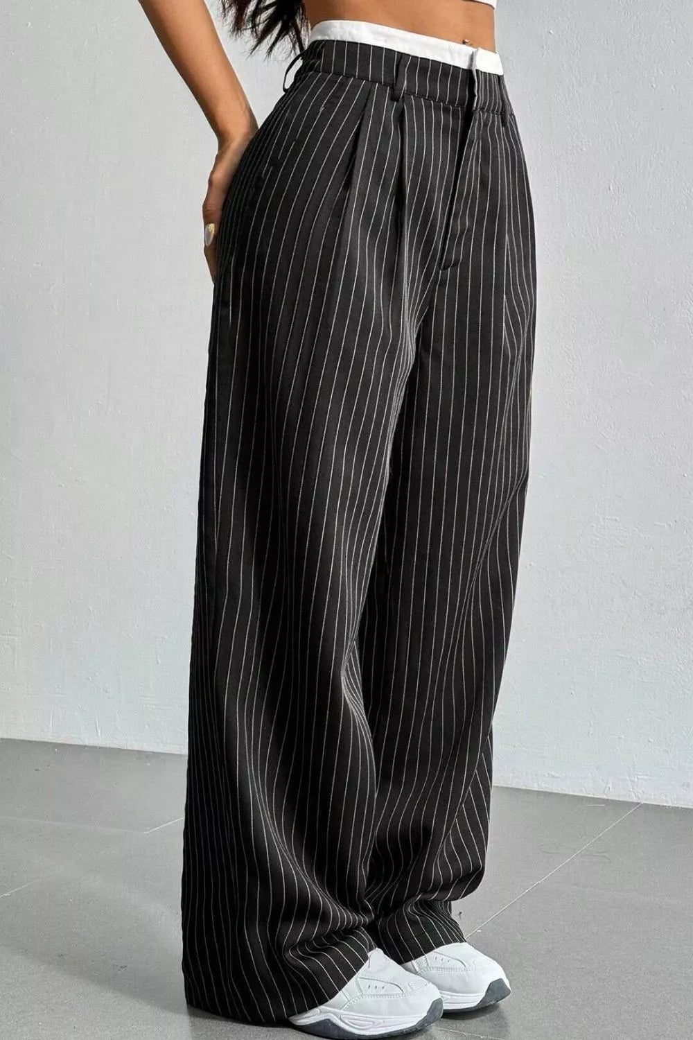 Black wide-leg pinstripe trousers with a white waistband, shown on a model from the waist down wearing white sneakers.