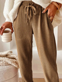Person wearing brown ribbed pants holding a white mug indoors.