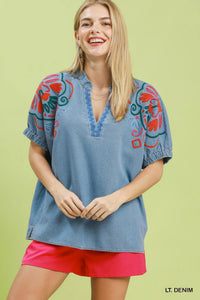 Woman wearing a light denim blouse with colorful embroidery on a green background