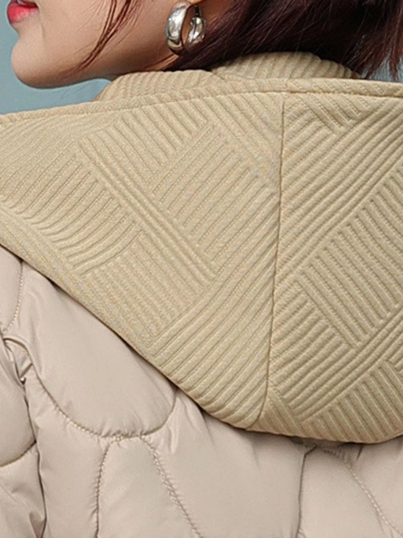 Close-up of a beige quilted puffer jacket with a large ribbed hood, worn by a model with dark hair and silver hoop earrings.