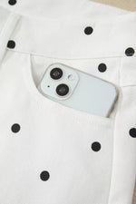 White smartphone with black camera lens on a white fabric background with black polka dots