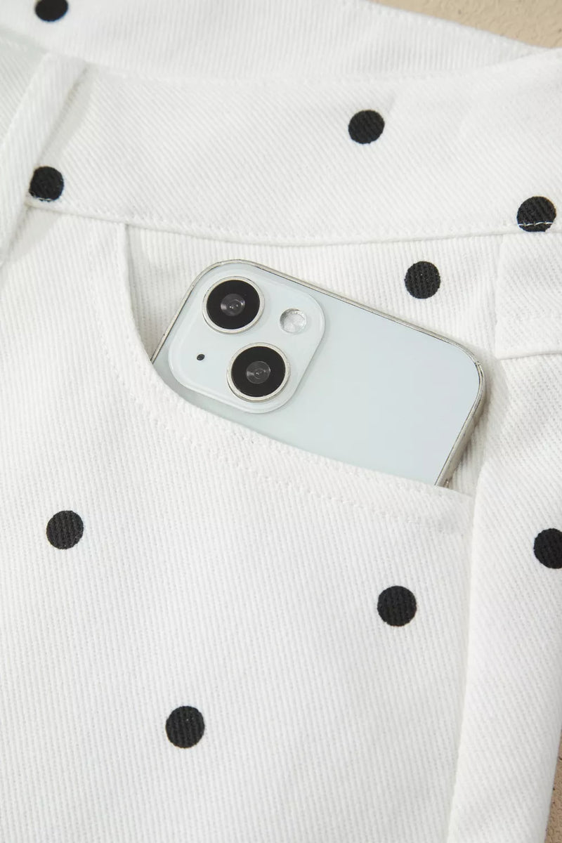 White smartphone with black camera lens on a white fabric background with black polka dots