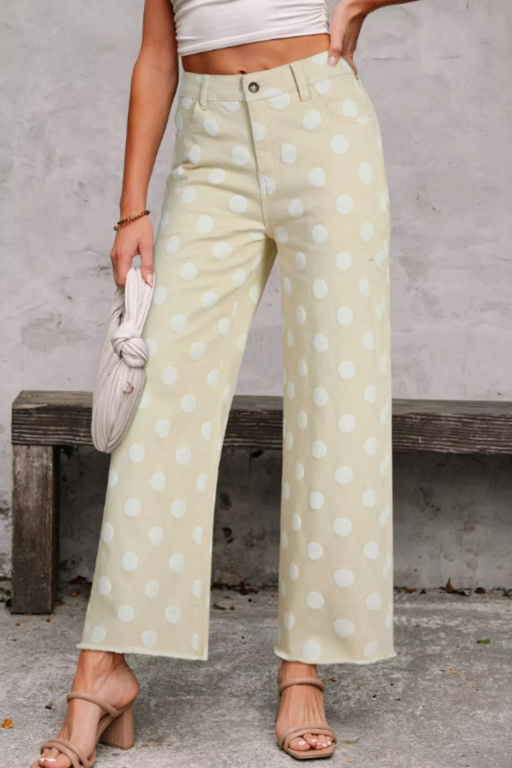 Person wearing light green pants with white polka dots, standing against a gray wall.