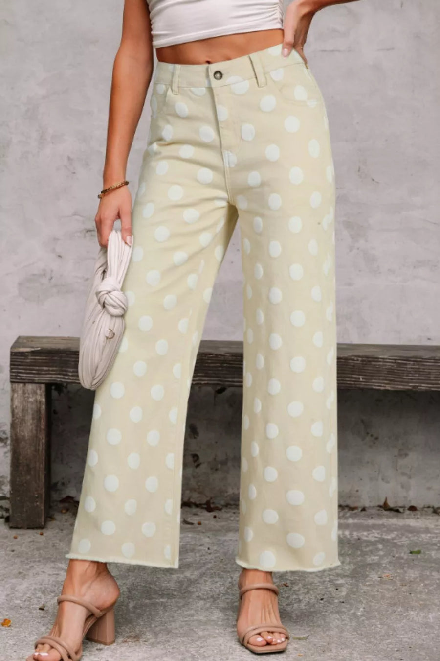 Person wearing light green pants with white polka dots, standing against a gray wall.