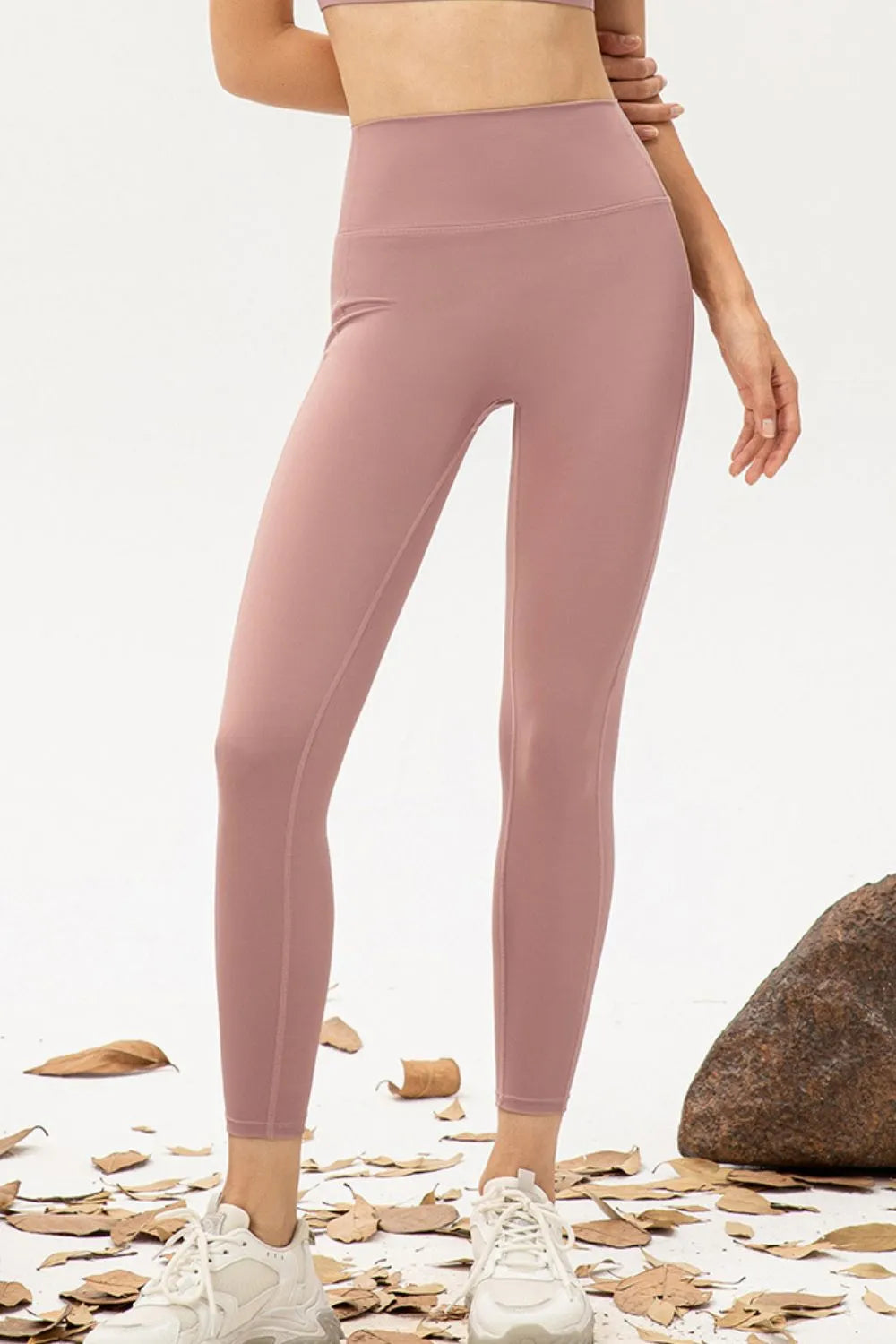 Person wearing pink leggings standing on a natural ground with rocks and leaves.