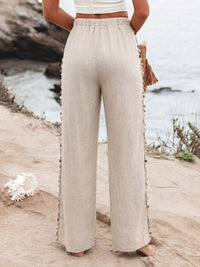 Person wearing beige wide-leg pants standing on a sandy beach.
