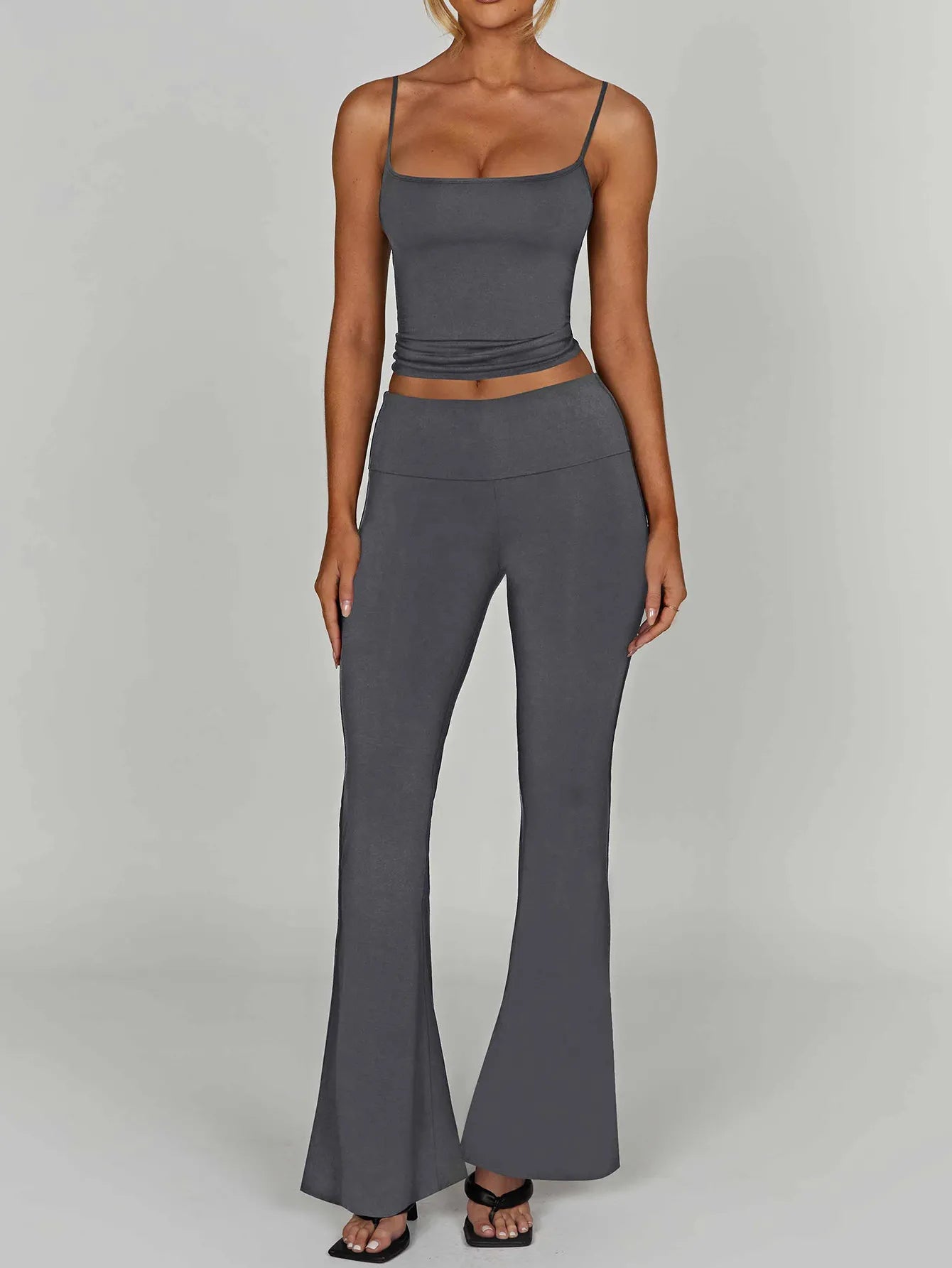 Woman wearing a gray tank top and high-waisted pants on a plain background