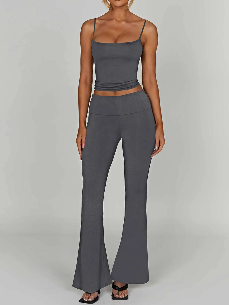 Woman wearing a gray tank top and high-waisted pants on a plain background