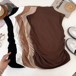 Three brown sleeveless tops on a white surface with a hand pointing to one of them.