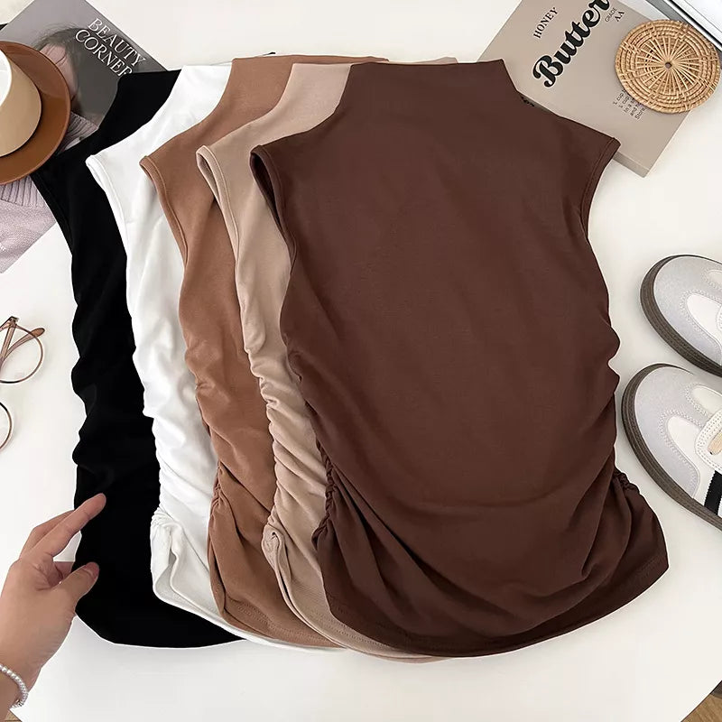Three brown sleeveless tops on a white surface with a hand pointing to one of them.
