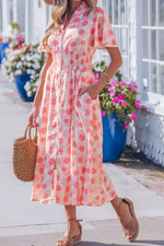 Woman wearing a pink polka dot dress with a straw bag in an outdoor setting.