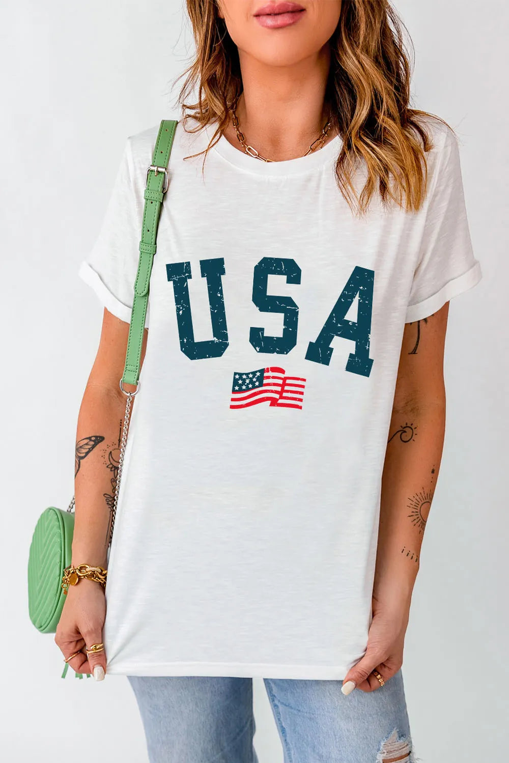 Person wearing a white t-shirt with 'USA' and an American flag graphic, holding a green handbag.