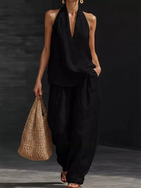 Person wearing a black outfit holding a woven bag against a dark background
