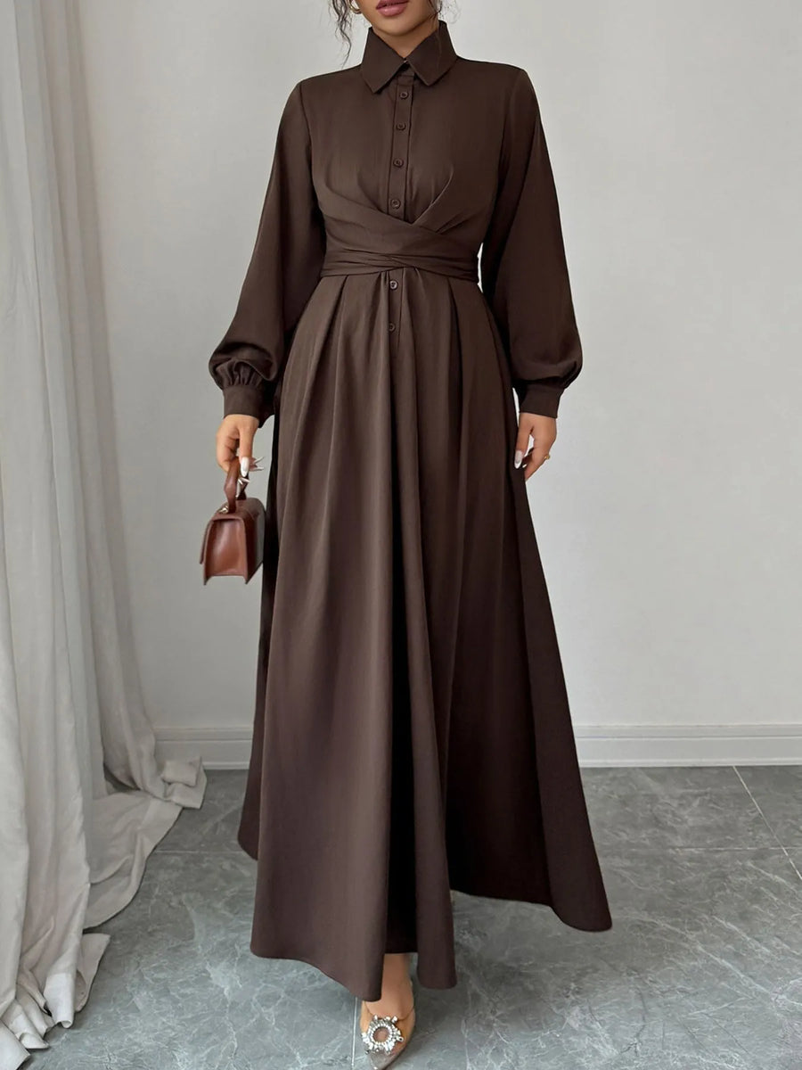 Woman wearing a long brown dress holding a matching handbag against a neutral background