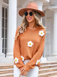 Woman wearing a brown sweater with white floral designs and a matching hat, standing outdoors.