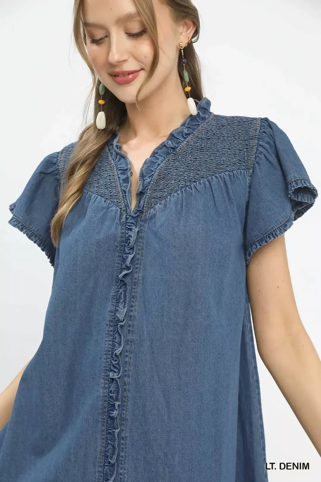 Woman wearing a blue denim dress with ruffled sleeves on a white background