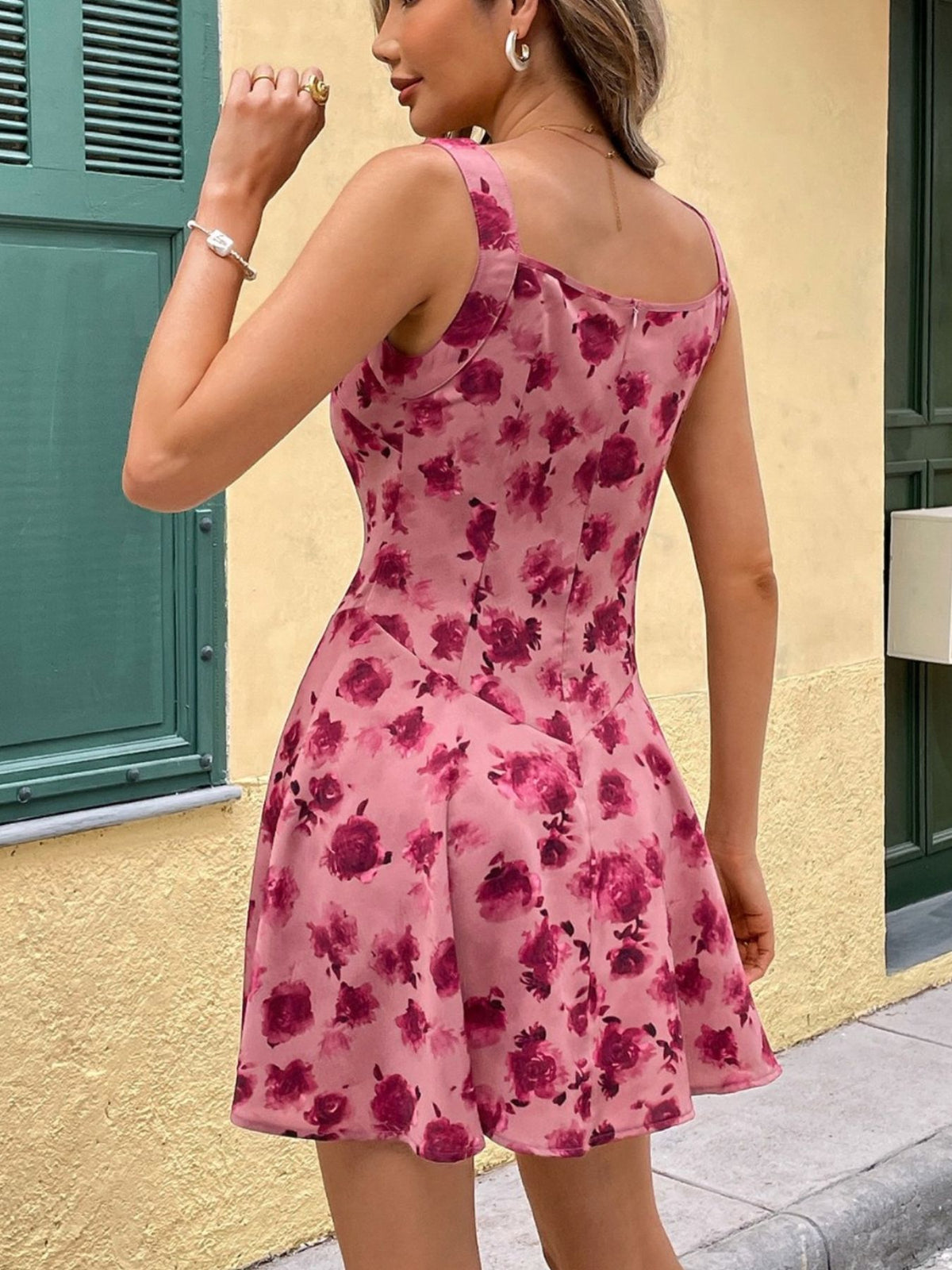 Woman wearing a pink floral dress standing against a yellow wall.
