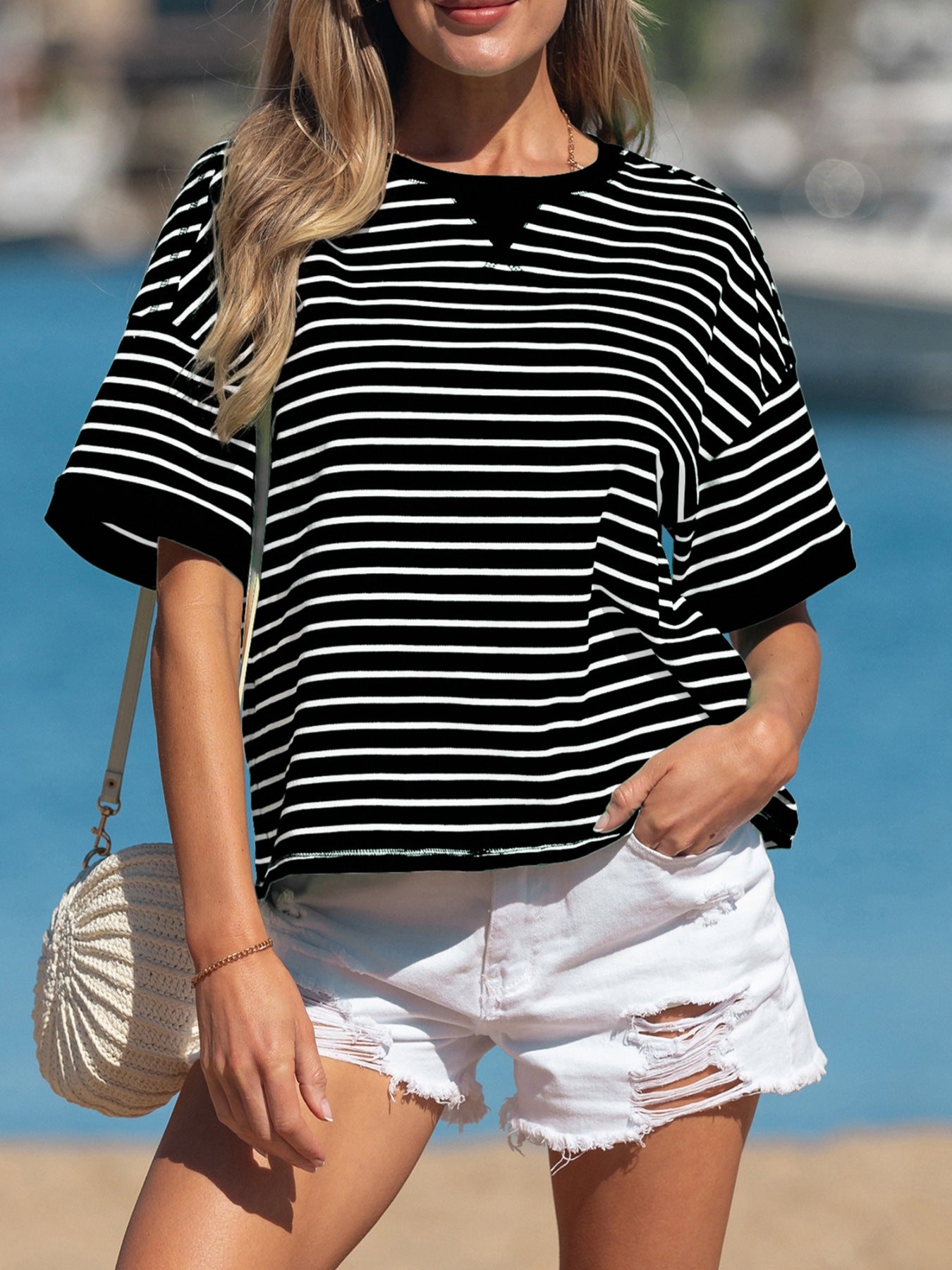 Woman wearing a black and white striped shirt and white shorts with a beach background