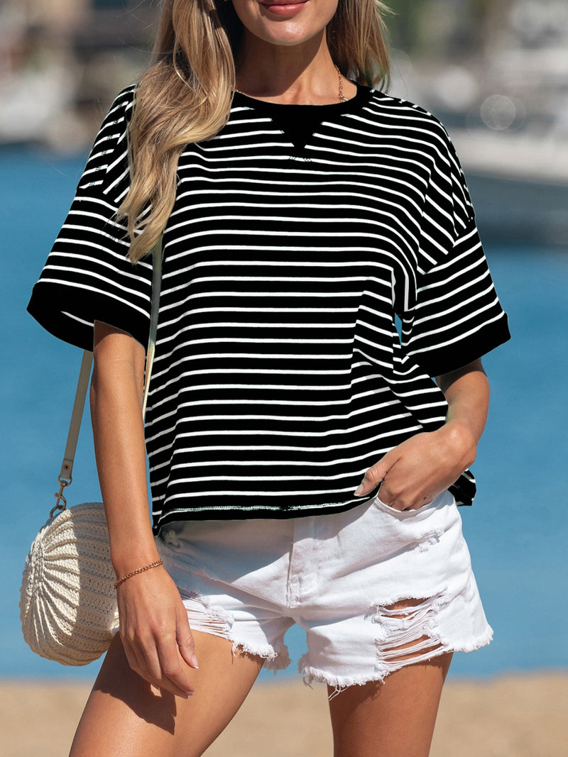 Woman wearing a black and white striped shirt and white shorts with a beach background
