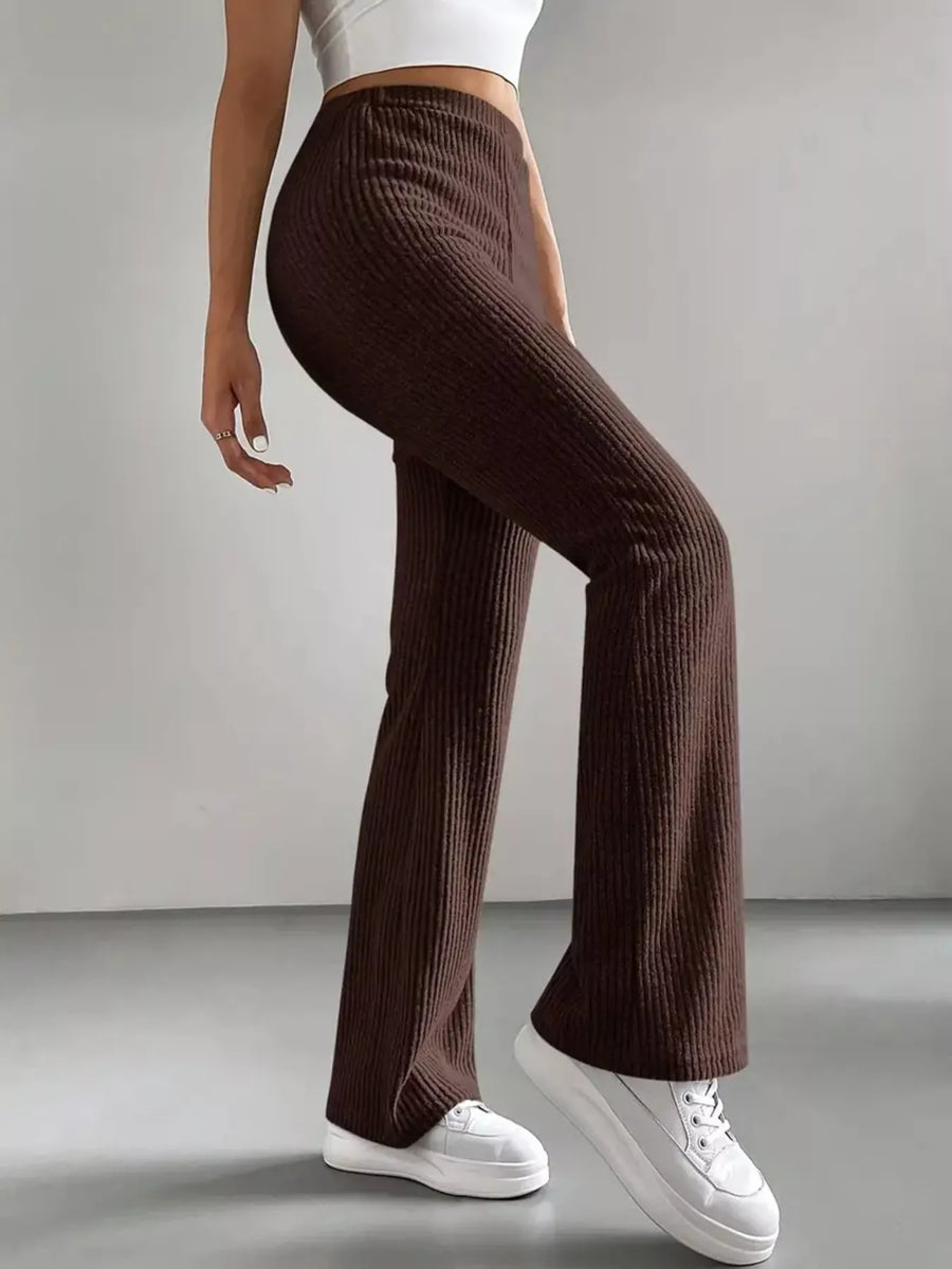 Person wearing brown ribbed pants and white sneakers on a plain background