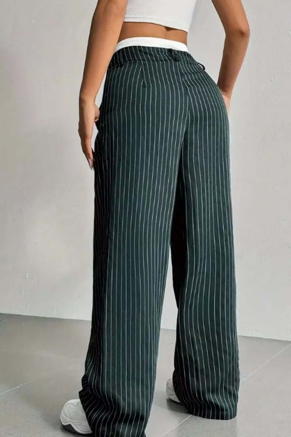 A person wearing dark green wide-leg pinstripe trousers with a white waistband, shown from the back in a studio setting.