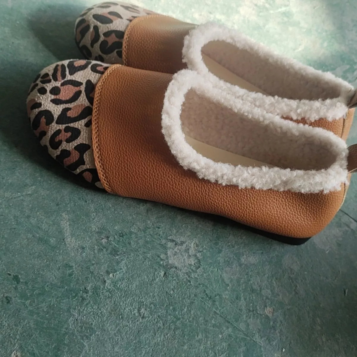 Pair of slippers with leopard print soles and white fleece lining on a green surface