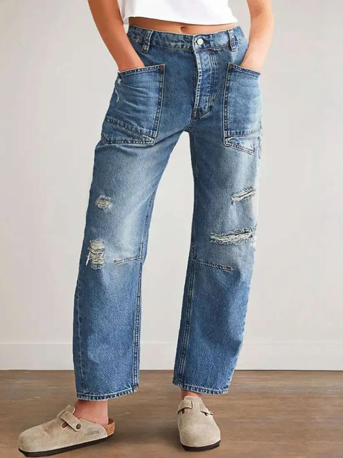 Person wearing distressed blue jeans with a plain background