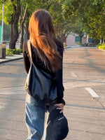 Person with long hair walking on a street with trees and buildings in the background