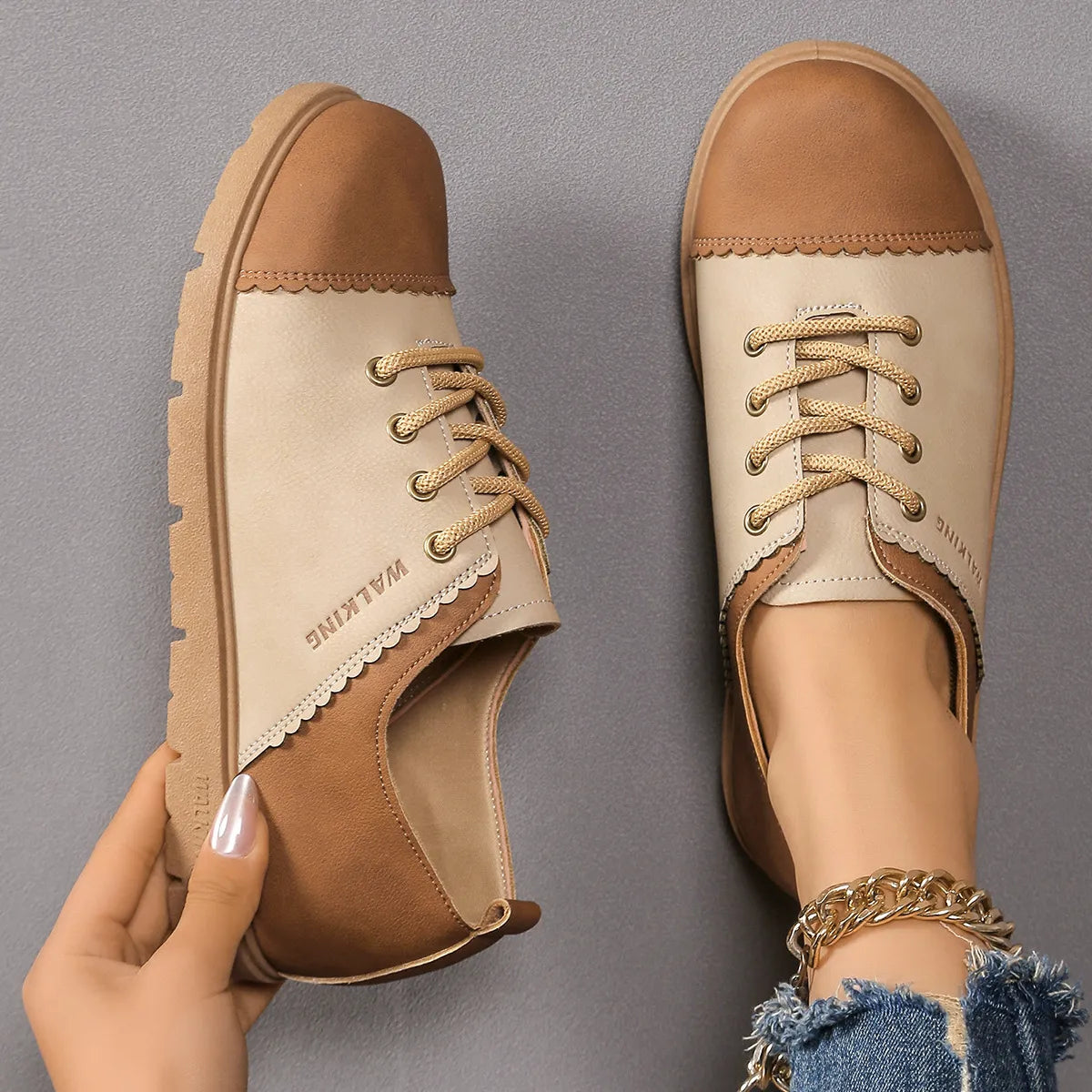 Pair of tan and beige shoes with a hand holding one shoe on a gray background