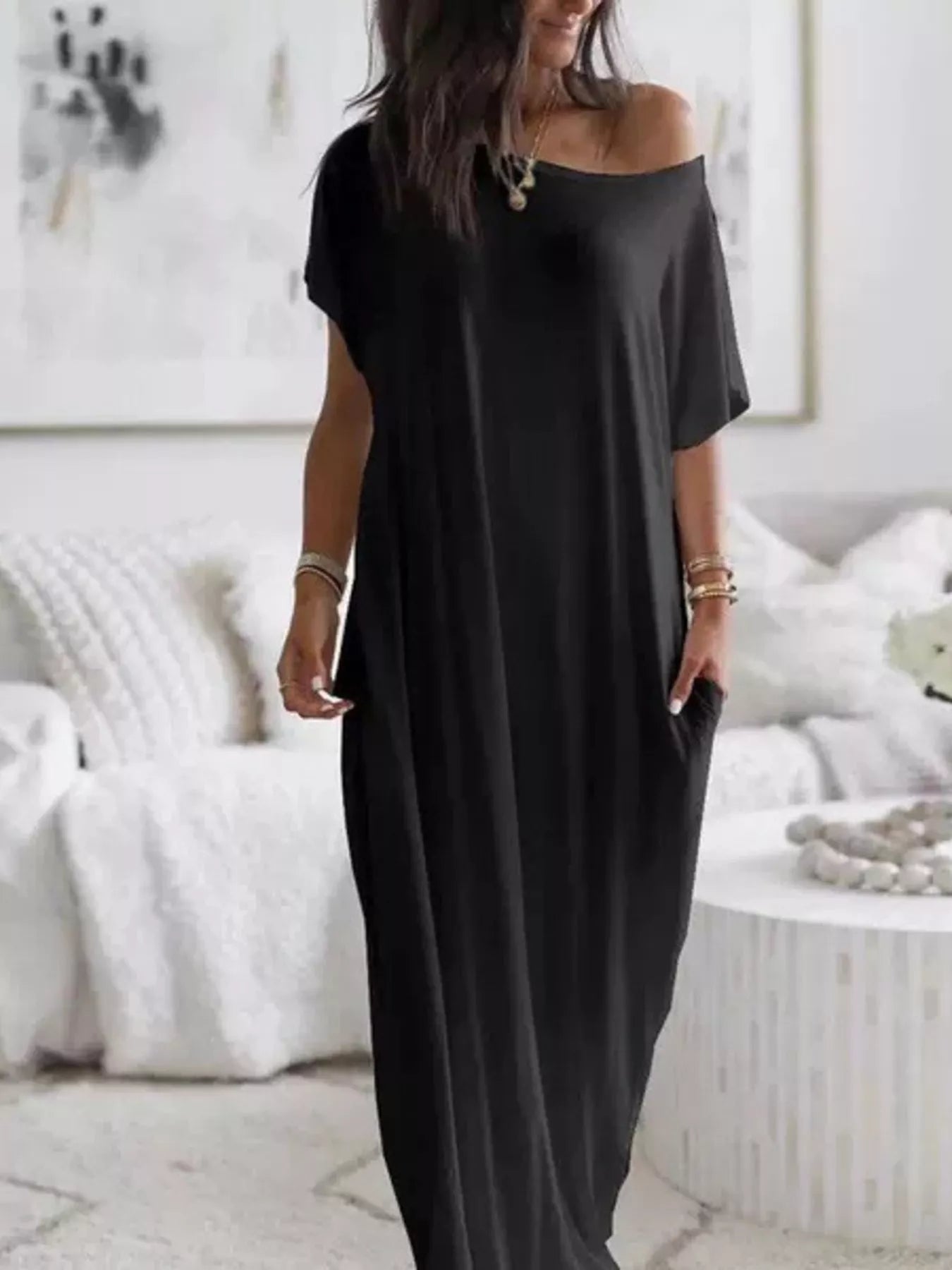 Woman wearing a black off-shoulder dress in a minimalistic room.