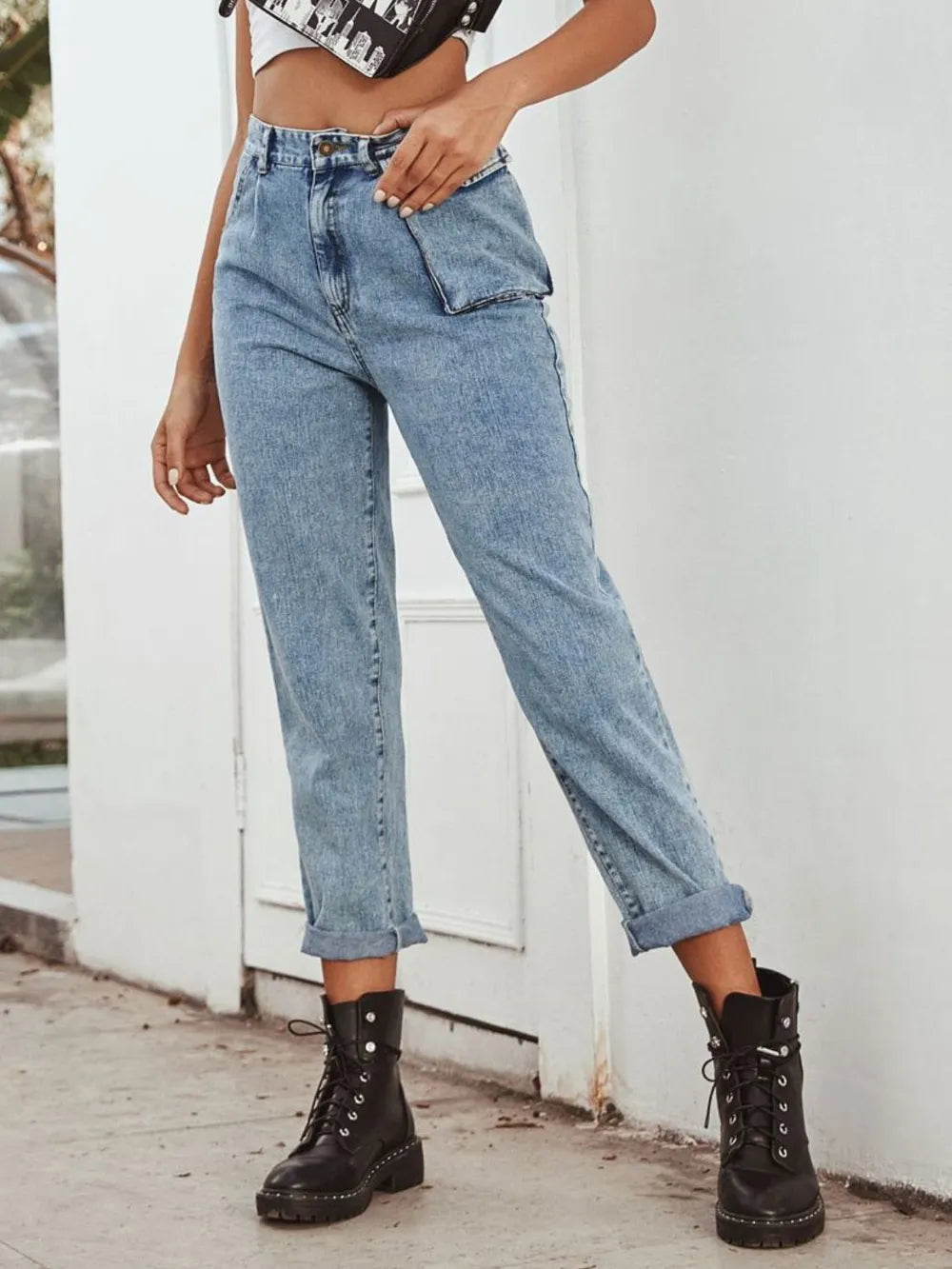 Person wearing high-waisted blue jeans and black boots against a white wall.