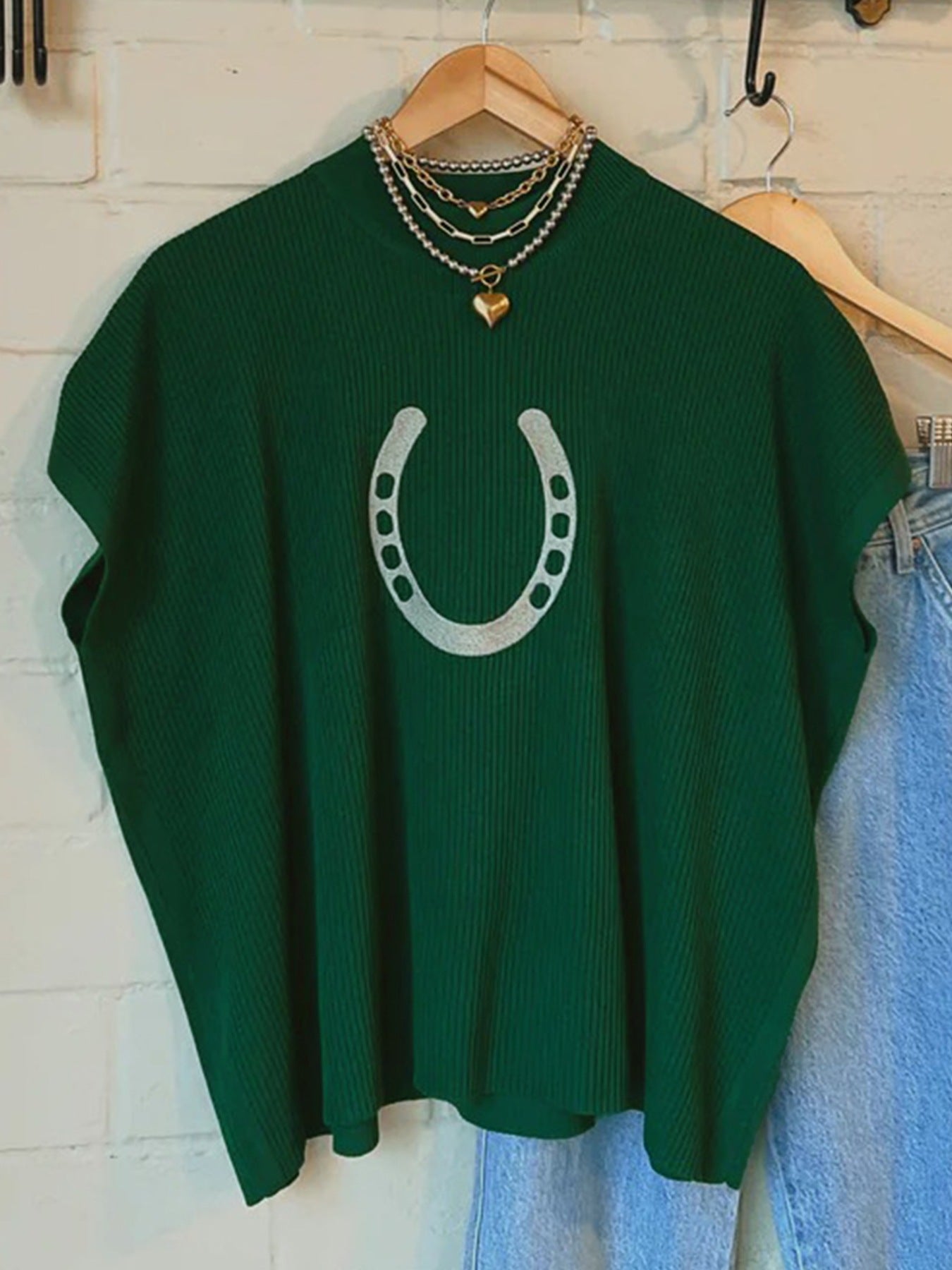 Green sweater with a horseshoe design on a hanger against a white wall.