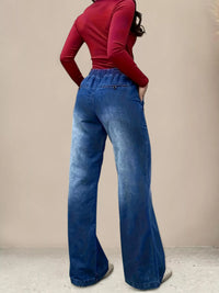 Person wearing blue wide-leg jeans and a red top against a beige background