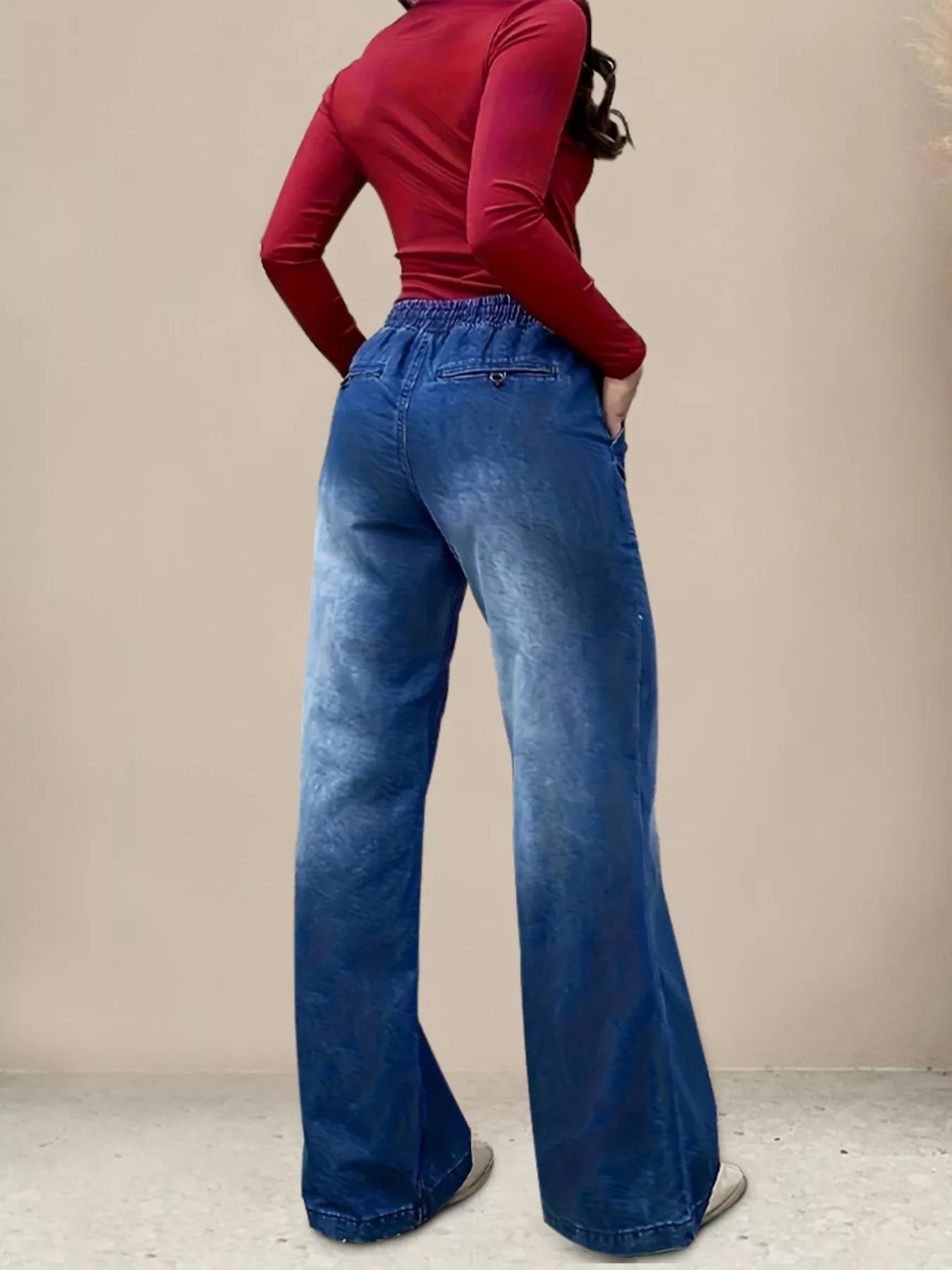 Person wearing blue wide-leg jeans and a red top against a beige background