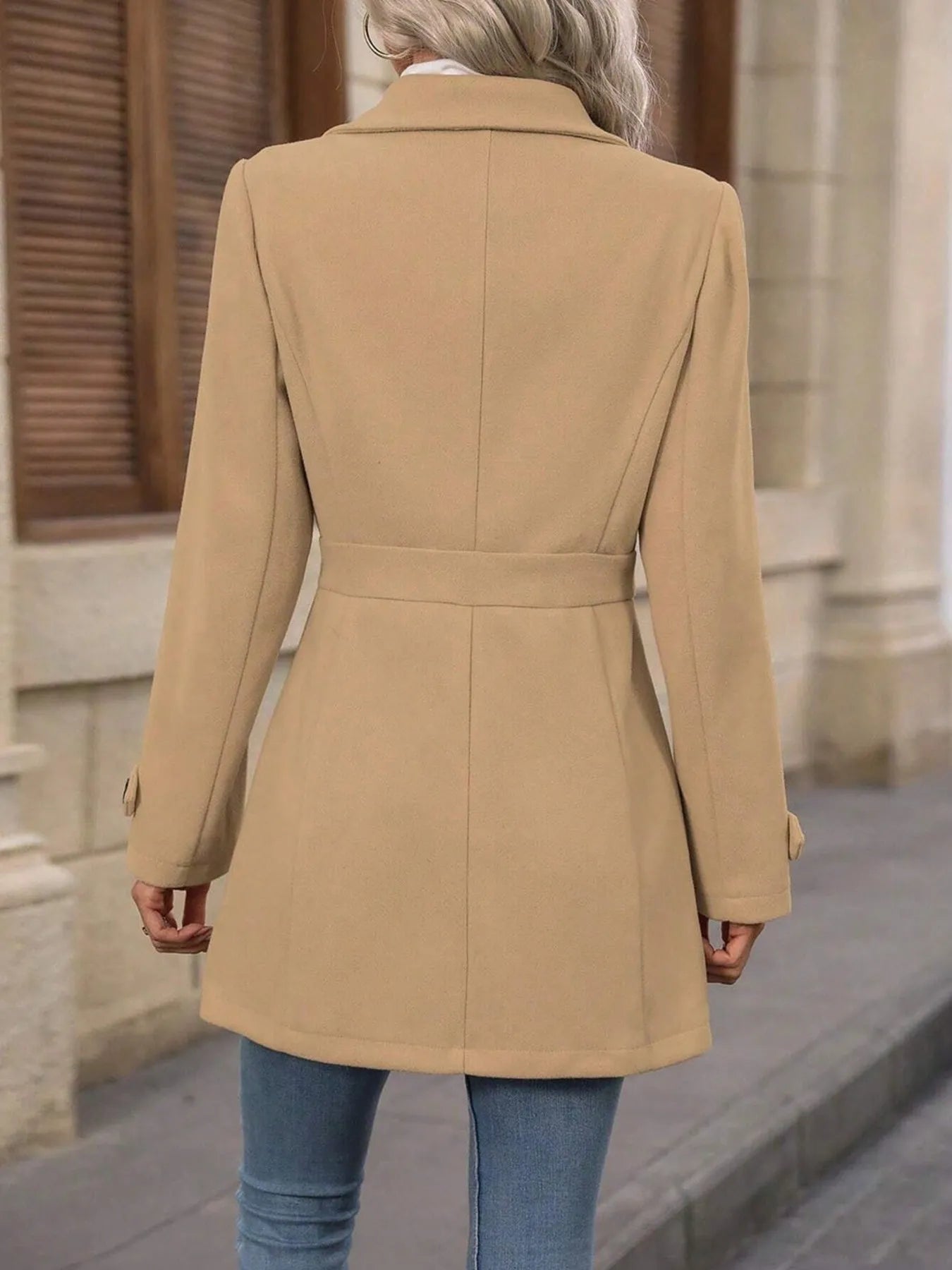 Person wearing a beige coat standing on a street.