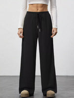 Person wearing black wide-leg pants and a white top on a plain background