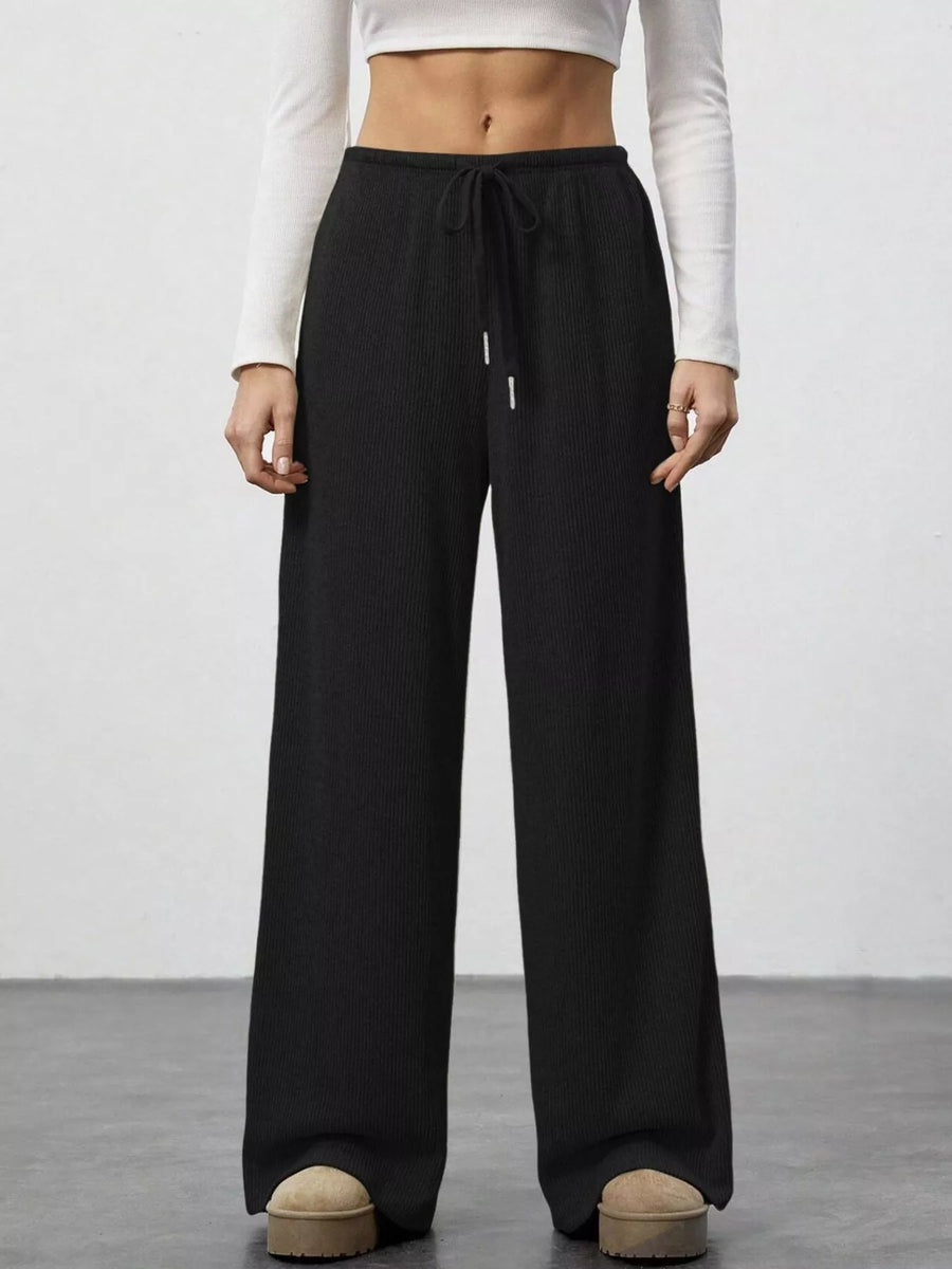 Person wearing black wide-leg pants and a white top on a plain background