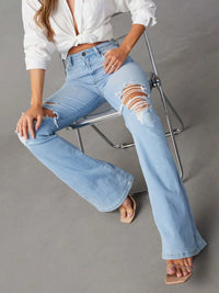 Person wearing light blue ripped jeans and a white shirt on a gray background